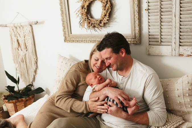 Newborn family pictures featuring parents cuddling comfortably on a bed with baby.