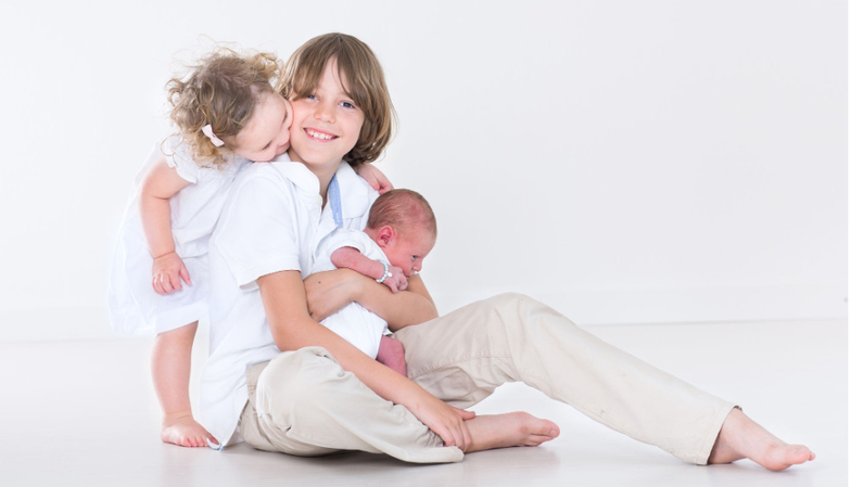 Newborn family pictures capturing older siblings interacting tenderly with the newborn.