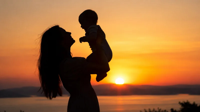 parent holding a baby securely in a sunset silhouette