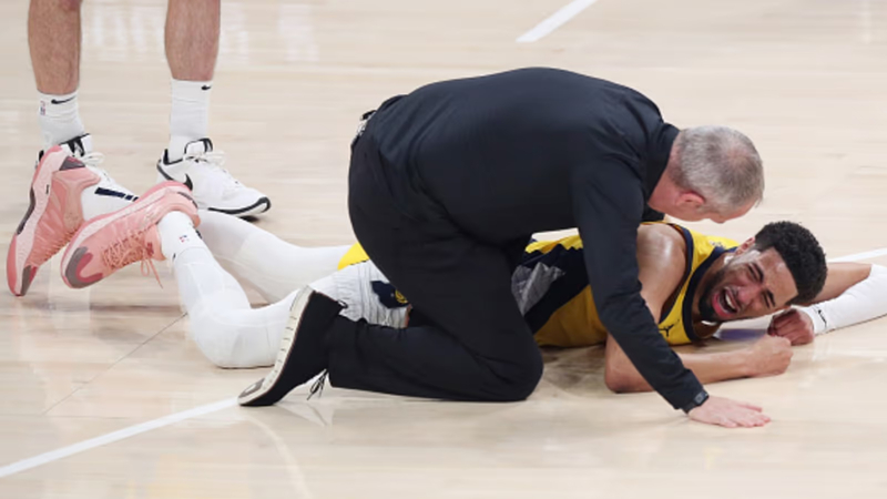 Tyrese Haliburton lying on the court in pain as a team staff member attends to him