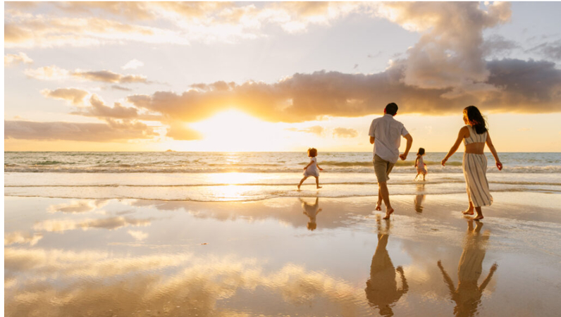 Classic family beach portrait with parents and children smiling on the shore.