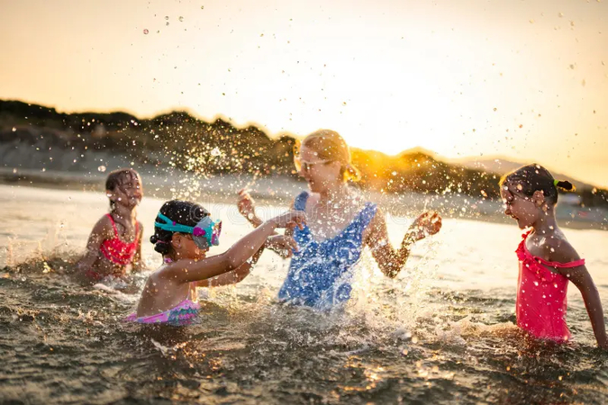 Candid family beach photo showing parents and children jumping in ocean waves.