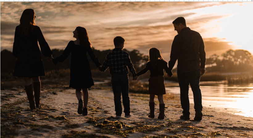 Golden hour silhouette of a family holding hands on the beach during sunset