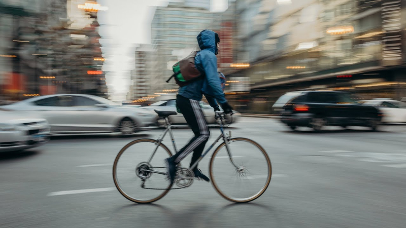 panning shot of a boy riding bicycle on a busy road